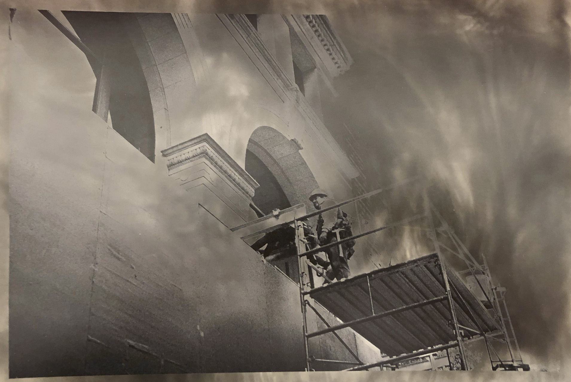 A person stands on top of scaffolding near a building facade in a solarized photograph